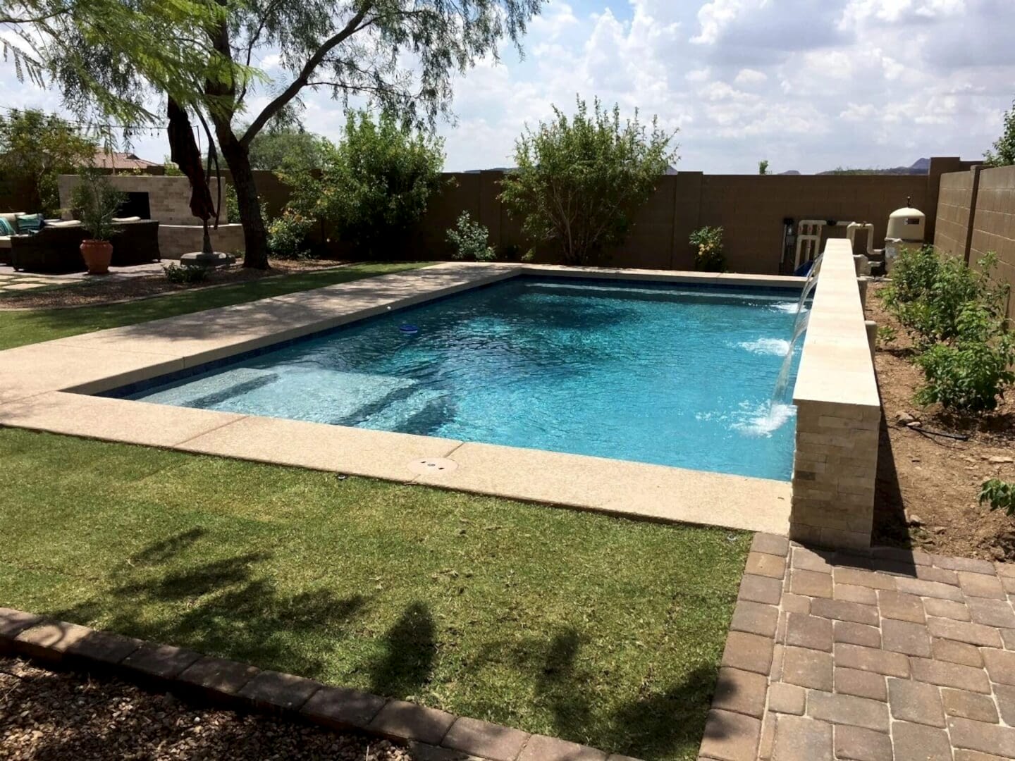 A pool with a stone wall and grass around it.