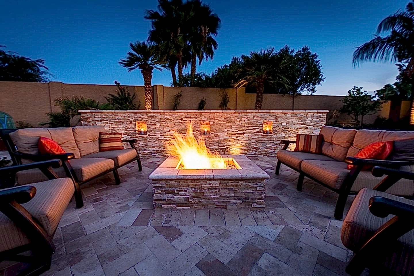 A fire pit with chairs around it and palm trees in the background.