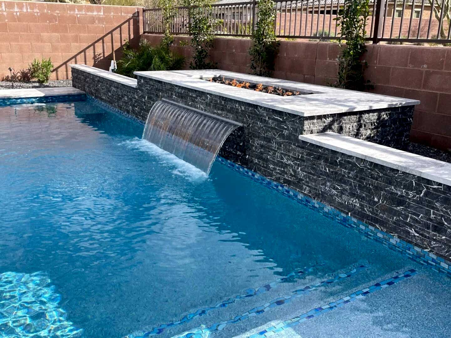 A pool with a waterfall and stone wall.