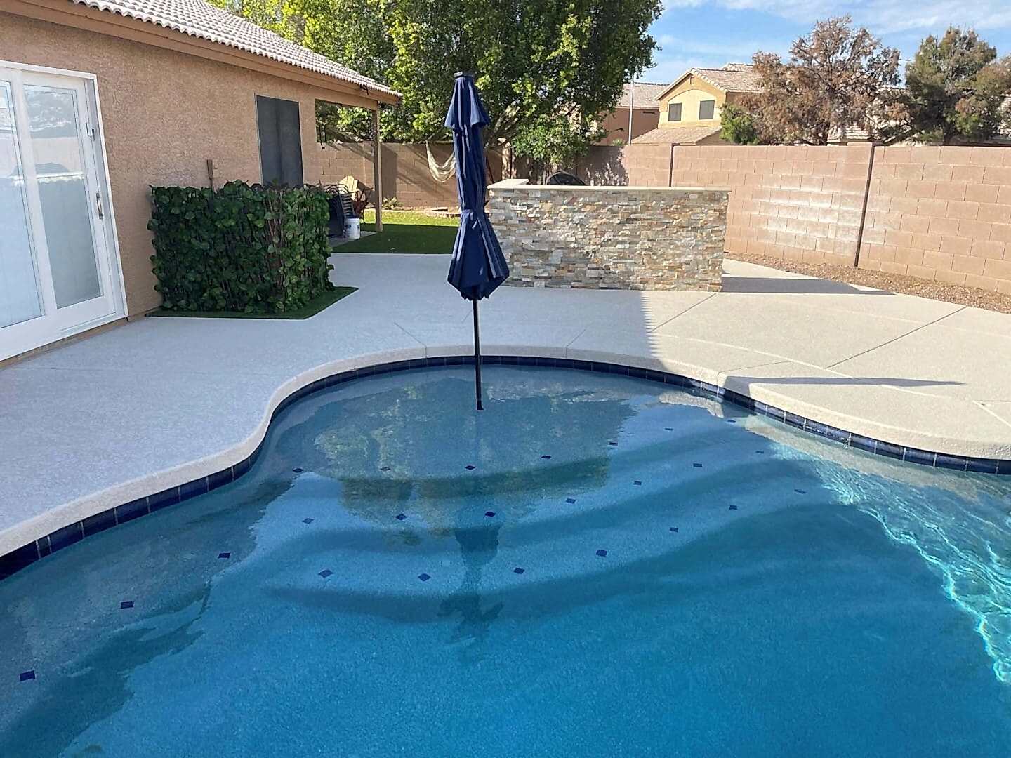 Here's an alt tag for the image: Pool with umbrella and stone wall.